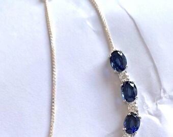 Op de afbeelding: Een zilveren kettingarmband met een rij ovale blauwe saffieren en kleine heldere diamanten.