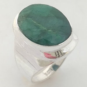 Op de afbeelding: Een zilveren ring met een grote, ovaalvormige, ondoorzichtige groene edelsteen in een gladde zetting. De ringband is breed en gepolijst, met een zichtbaar 925-keurmerk gestempeld op de binnenzijde, wat duidt op een samenstelling van sterling zilver.