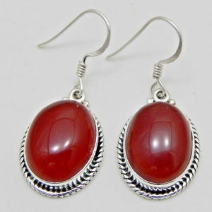 May include: A pair of silver dangle earrings. Each earring features a large, oval, polished, red gemstone set within a decorative silver frame. The earrings have a simple hook design for pierced ears.