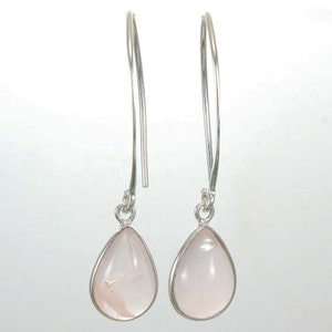 May include: A pair of dangle earrings featuring teardrop-shaped, pale pink gemstones set in silver-colored metal. The earrings have long, curved ear wires, creating a delicate and elegant design. The gemstones appear translucent, with subtle variations in color.