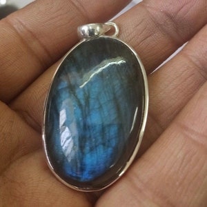 Puede incluir: Colgante de labradorita ovalado con bisel plateado. La piedra preciosa muestra una iridiscencia azul y turquesa vibrante. El colgante tiene un pequeño lazo en la parte superior para una cadena.