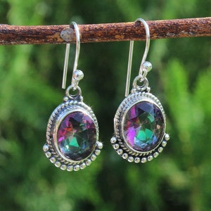 May include: A pair of sterling silver dangle earrings. Each earring features an oval, multi-colored gemstone with a rainbow effect, set within a detailed silver frame. The earrings are suspended from a simple hook.