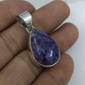May include: A teardrop-shaped pendant with a polished, vibrant purple stone. The stone is encased in a silver metal setting with a matching bail for a necklace chain. The stone's color has swirls of white and dark purple.