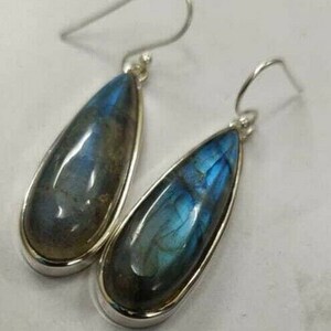 May include: A pair of teardrop-shaped earrings with iridescent blue and green stones set in silver-colored metal. The earrings have a hook closure. The stones have a polished, glossy finish.
