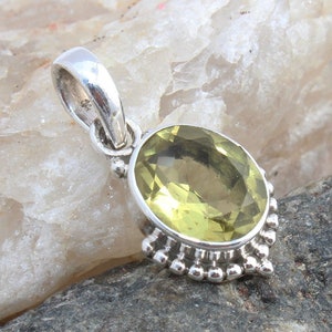 May include: A silver pendant with an oval, light yellow gemstone. The gemstone is set in a silver bezel with a decorative beaded edge. The pendant has a silver loop for a chain.