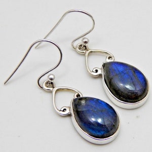 Puede incluir: Un par de pendientes de plata con piedras de labradorita azul iridiscente en forma de lágrima. Las piedras están engastadas en un bisel de plata y suspendidas de un gancho decorativo de plata.