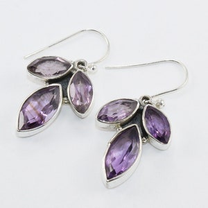 Puede incluir: Un par de pendientes de plata con tres piedras de amatista moradas en forma de marquesa. Las piedras están engastadas en un bisel de plata y dispuestas en un diseño de racimo. Los pendientes tienen un cierre de gancho sencillo.