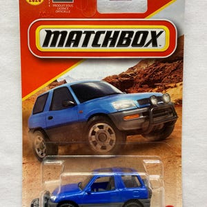 May include: A Matchbox toy car on a red and orange card. The toy car is a blue SUV with black accents. The card has the Matchbox logo and the Toyota logo. The card also has the text "NEW NOUVEAU 2020".