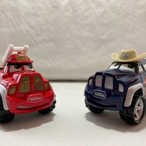May include: Two Tonka toy vehicles, one red fire truck with a white ladder and one dark blue sheriff SUV with a beige cowboy hat on top. Both vehicles feature large black tires, white wheel wells, and expressive eyes on the windshields.