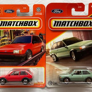 May include: Two Matchbox die-cast toy cars, a red Ford Fiesta MK2 and a green Ford Fiesta MK2, on their packaging. The packaging is red and white with the Matchbox logo and the words "New" and "2024".