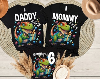 May include: Three black t-shirts featuring a dinosaur graphic and text. The shirts read "Daddy Rawr!" "Mommy Rawr!" and "Rawr! I'm 6".