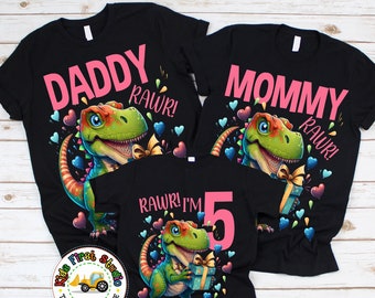 May include: Three black t-shirts featuring a dinosaur graphic and the words "Daddy Rawr!" "Mommy Rawr!" and "Rawr! I'm 5" in pink text.