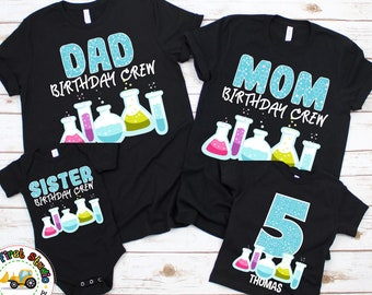 May include: A set of four black t-shirts with a science theme. The shirts feature the words "Dad Birthday Crew", "Mom Birthday Crew", "Sister Birthday Crew", and "5 Thomas". Each shirt has a graphic of colorful beakers and test tubes.