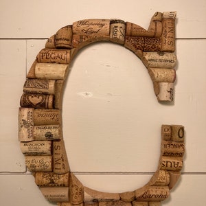May include: A large letter C made from wine corks. The corks are arranged in a circle, with the letter C formed by the space between the corks. The corks are all different colors and have different labels on them.