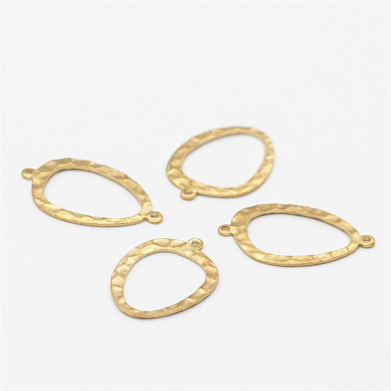 May include: Four gold-toned metal oval-shaped pendant charms with a hammered texture and jump rings.