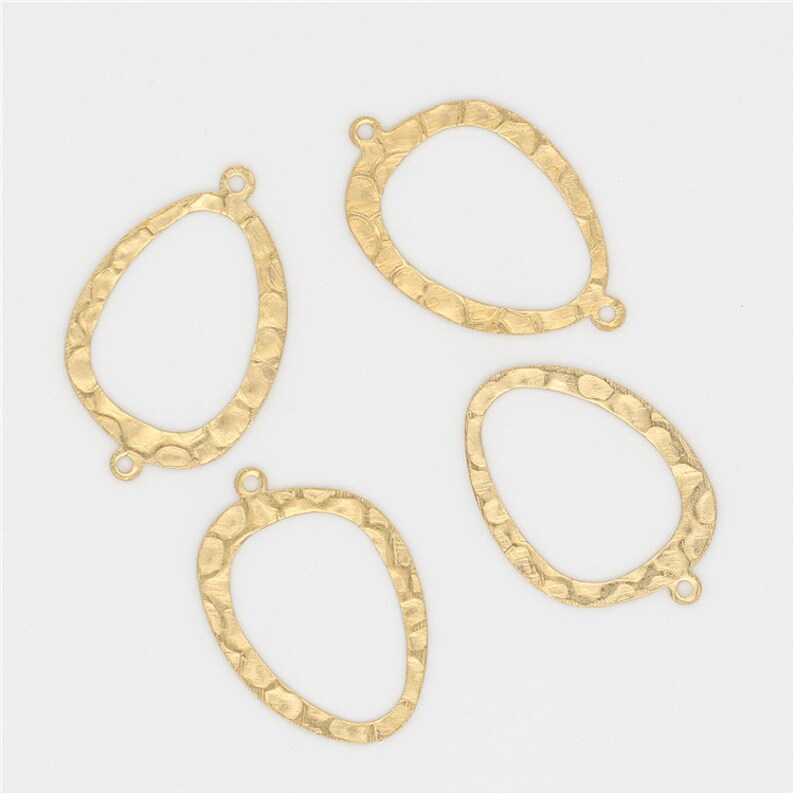 May include: Four gold-toned metal oval-shaped pendant blanks with a textured surface. Each blank has two small holes at the top for attaching a jump ring or other jewelry findings.