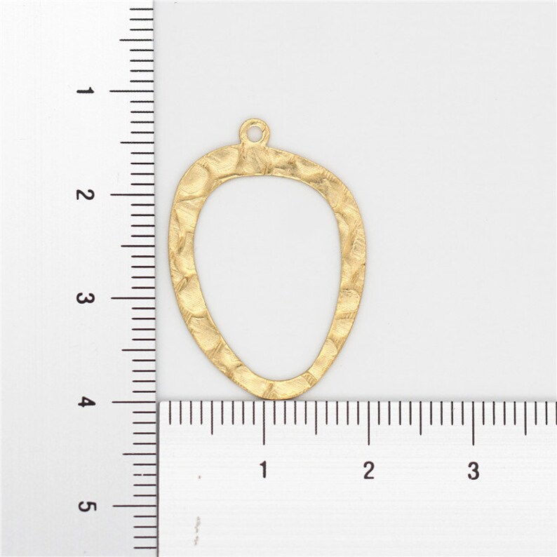 May include: Gold-toned metal pendant shaped like an oval with a textured surface. The pendant measures approximately 2 inches in height and 1.5 inches in width.