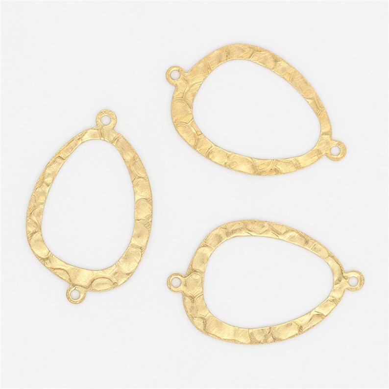 May include: Three gold-toned metal oval-shaped pendant blanks with a textured surface. Each blank has two jump rings attached.