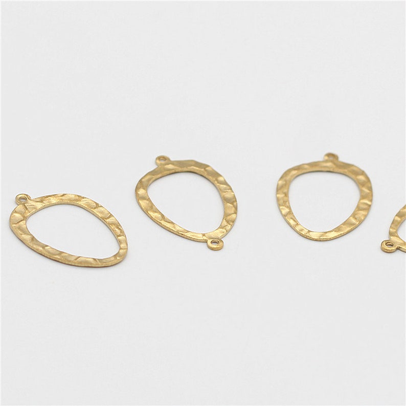 May include: Four gold-toned metal oval-shaped pendant charms with a hammered texture. Each charm has two small loops at the top.