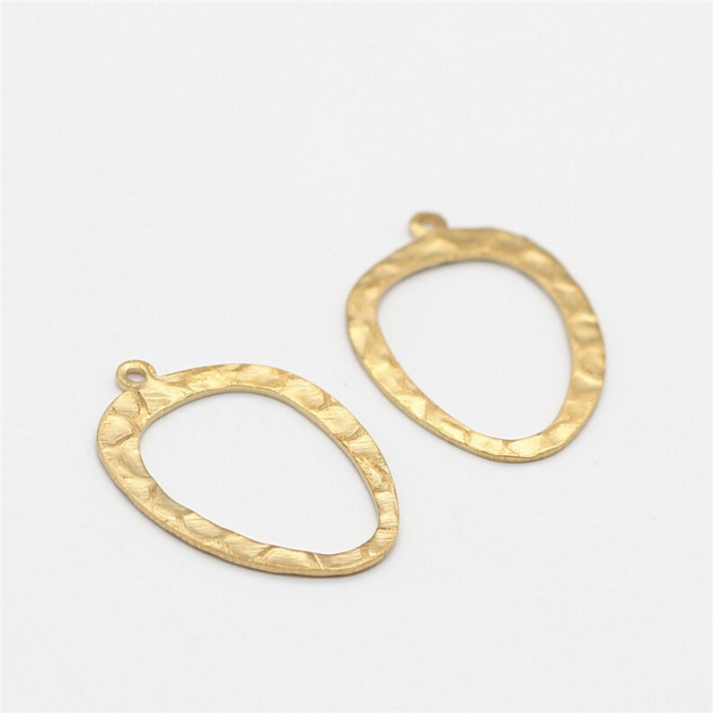 May include: Two gold-toned metal earring blanks with a hammered texture and a rounded oval shape. Each blank has a small loop at the top for attaching earring wires.