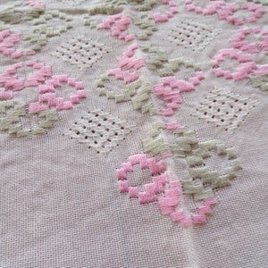 May include: Close-up of a white fabric with pink and green embroidered flowers. The fabric has a delicate, lacy texture.