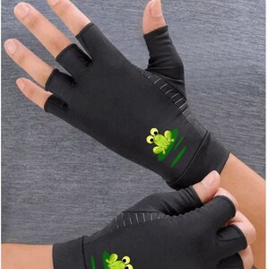 K&ouml;nnte beinhalten: Ein Paar schwarze Fingerlose Handschuhe mit einem gr&uuml;nen Frosch-Design auf jedem Handschuh. Der Frosch hat gro&szlig;e Augen und sitzt auf einem gr&uuml;nen Seerosenblatt.