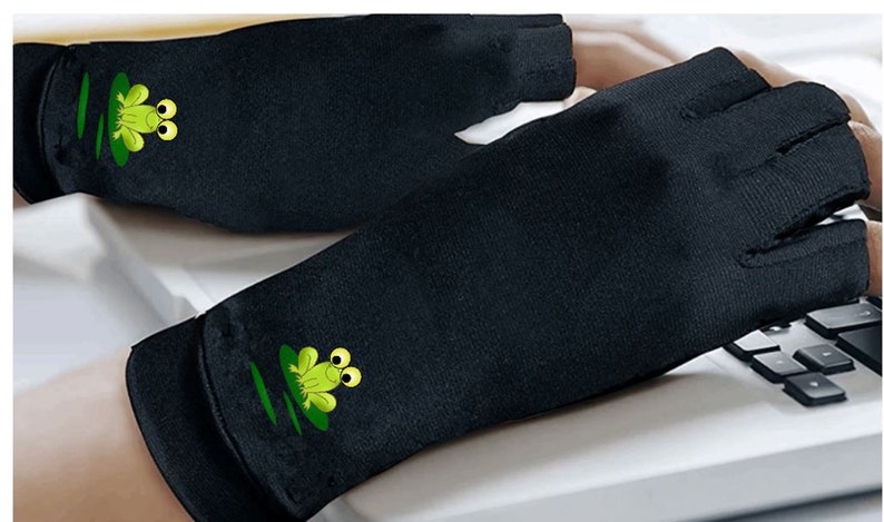 K&ouml;nnte beinhalten: Paar schwarze fingerlose Handschuhe mit einem gr&uuml;nen Froschdesign auf jedem Handschuh. Die Handschuhe sind aus einem weichen, atmungsaktiven Stoff gefertigt und sollen helfen, Handm&uuml;digkeit zu reduzieren.