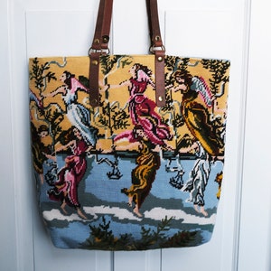 May include: A yellow and blue tapestry tote bag with brown leather straps. The tapestry features a colorful scene of people dancing in a garden.
