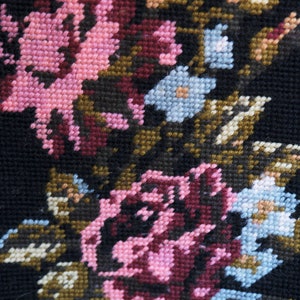 May include: Close-up of a black fabric with embroidered pink, blue, and brown flowers. The fabric has a textured, woven appearance.