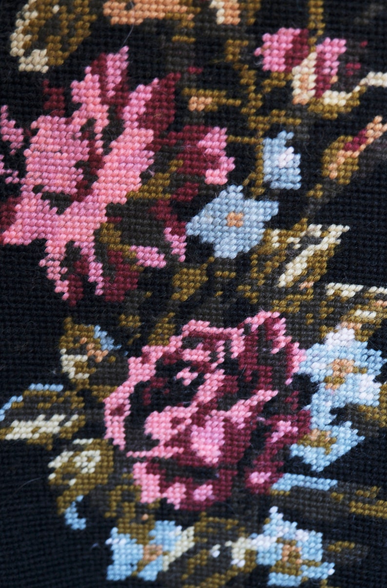 May include: Close-up of a black fabric with embroidered pink, blue, and brown flowers. The fabric has a textured, woven appearance.