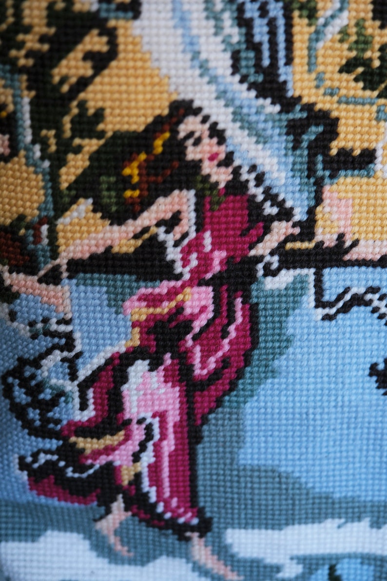 May include: A close-up of a colorful needlepoint embroidery depicting a woman in a pink and purple dress with a blue background.