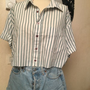 Peut inclure: Une chemise boutonn&eacute;e &agrave; manches courtes, &agrave; rayures blanches et vertes, coup&eacute;e au niveau de la taille. La chemise est port&eacute;e sur un short en jean bleu clair.