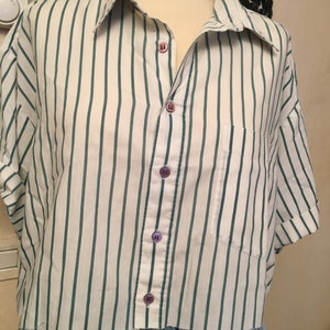 Peut inclure: Une chemise &agrave; manches courtes boutonn&eacute;e &agrave; rayures blanches et vertes avec une poche sur le c&ocirc;t&eacute; gauche. La chemise a une ourlet court et est faite d'un tissu l&eacute;ger.