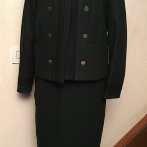 May include: A dark green skirt suit with a black trim and silver buttons. The jacket has a double-breasted closure.