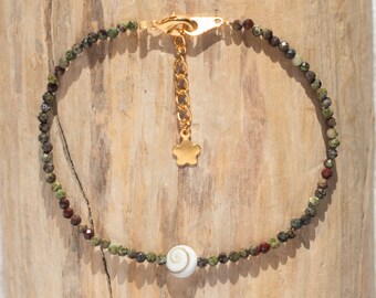 May include: A delicate gold chain bracelet with a small star charm and a white shell bead. The bracelet is made with small green and red gemstone beads.