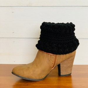 May include: A tan leather ankle boot with a black crocheted boot cuff. The boot has a block heel and a side zipper. The cuff is made of a thick, textured yarn and adds a stylish touch to the footwear.