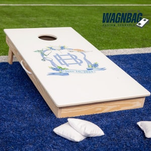 Custom cornhole boards featuring a white wooden cornhole board with a blue and white monogram and the date June 10, 2023. Displayed on blue artificial grass with two white bean bags. Perfect as custom logo boards, monogram cornhole, monogram corn hole, custom game board, custom boards, cornhole board, corn hole boards, cornhole score board, backyard games, groomsman gift and wedding decal.