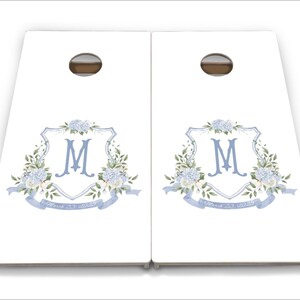 May include: A set of two white wooden cornhole boards featuring a blue and white floral design with the letter "M" in the centre. The boards have a blue ribbon with the text "Forever & Always" on them.