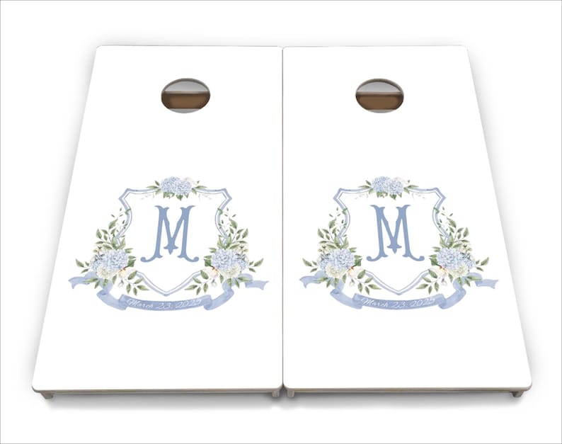 May include: A set of two white wooden cornhole boards featuring a blue and white floral design with the letter "M" in the centre. The boards have a blue ribbon with the text "Forever & Always" on them.