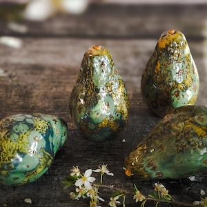 Può includere: Quattro pere in ceramica in tonalità di verde e marrone con una glassa screziata. Le pere sono disposte su una superficie di legno.