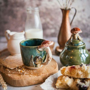 K&ouml;nnte beinhalten: Ein Set aus drei Keramikbechern mit gesprenkelter, matter Oberfl&auml;che. Die Becher sind in Creme-, Hellgrau- und Dunkelgraut&ouml;nen gehalten. Jeder Becher hat ein schlichtes, minimalistisches Design.