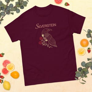 May include: Burgundy t-shirt with a graphic of a crow with a skull and roses. The text "SILVERSSTEIN" is printed in white above the graphic.