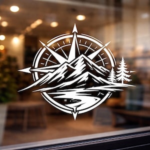 Può includere: Design a rosa dei venti bianca con montagne, alberi e un fiume. Il design è circolare e presenta un'illustrazione dettagliata di una catena montuosa, un fiume e due pini. La bussola punta verso le direzioni cardinali.