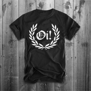 以下が含まれることがあります： 白い「Oi!」の文字が書かれた月桂樹の輪のデザインが施された黒いTシャツ