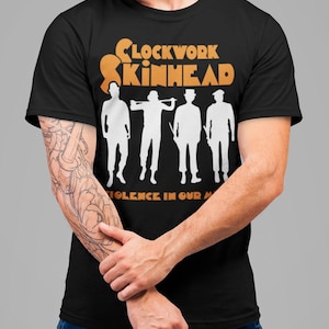 May include: Black t-shirt with a white graphic of four figures in silhouette. The text "Clockwork Skinhead" is in orange above the figures and "Violence in our minds" is in orange below the figures.