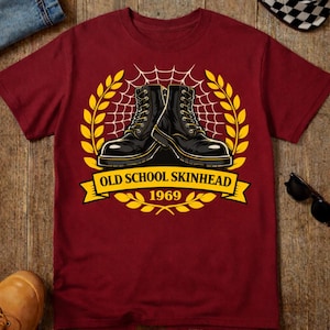 Puede incluir: Camiseta granate con un diseño de dos botas militares negras, una telaraña y una pancarta amarilla con la inscripción "OLD SCHOOL SKINHEAD 1969". El diseño está enmarcado por hojas de laurel amarillas.