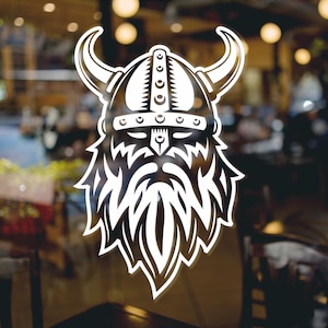 Op de afbeelding: Een witte vinyl sticker van het hoofd van een Viking krijger met een gehelmde helm en een lange baard. De sticker zit op een glazen deur met een wazige achtergrond van een restaurant interieur.