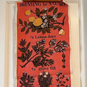 May include: A vintage kitchen tea towel with a red background and a recipe for salad dressing. The recipe includes 1/3 lemon juice, 2/3 olive oil, sprigs of fresh herbs, salt, and pepper. The towel features illustrations of lemons, olives, thyme, chives, and marjoram.