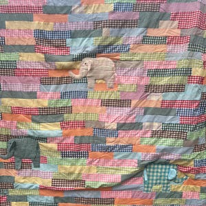 May include: A patchwork quilt with a colorful checkered pattern. The quilt features three appliqued elephant figures in different colors and sizes.