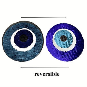 May include: Reversible sequin pillow with a blue evil eye design. One side is blue and white, the other side is purple and blue.